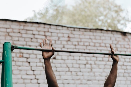 Hands of a person doing a pull-up on a metal bar against a brick wall.