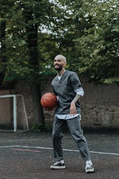 Smiling man in casual wear plays basketball outdoors on a court.