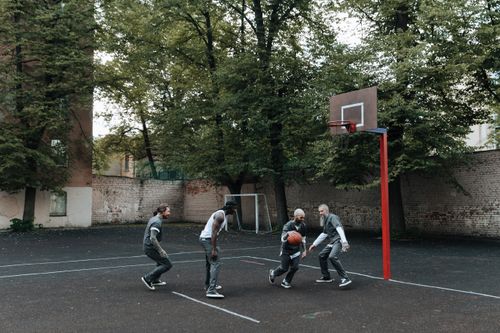 Free Inmates play a basketball game on an outdoor prison court surrounded by trees. Stock Photo