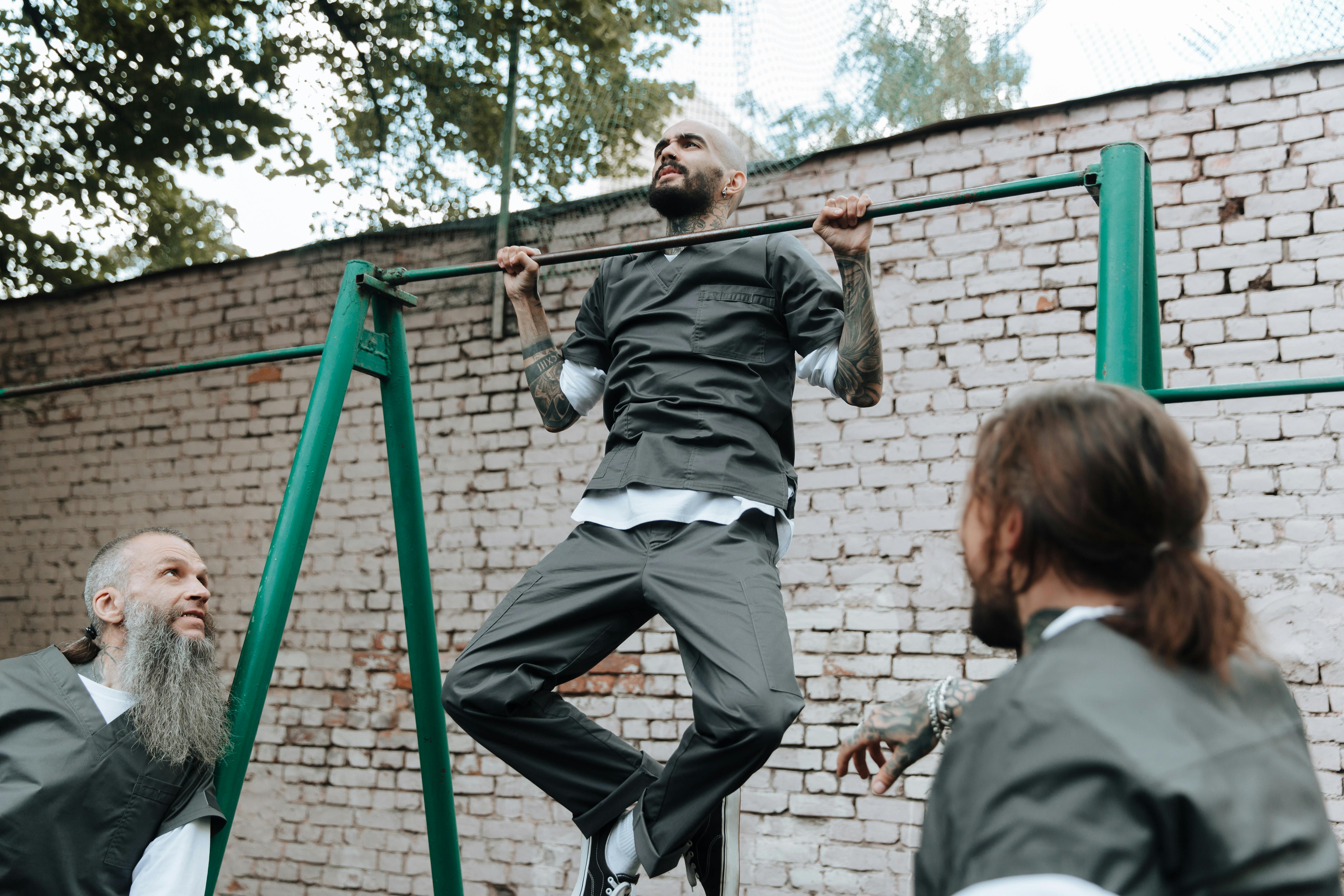 A group of men performing pull-ups on outdoor bars, demonstrating teamwork and fitness motivation.