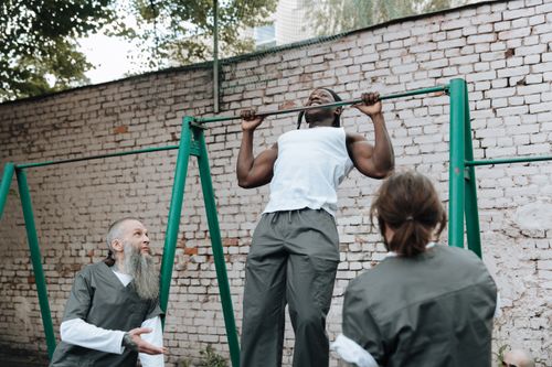 Free Outdoor workout session with men doing pull-ups on a bar, focusing on fitness and teamwork. Stock Photo
