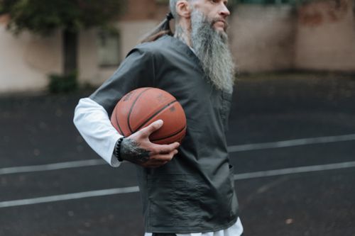 Free Bearded man holding a basketball on an outdoor court, embodying style and athleticism. Stock Photo
