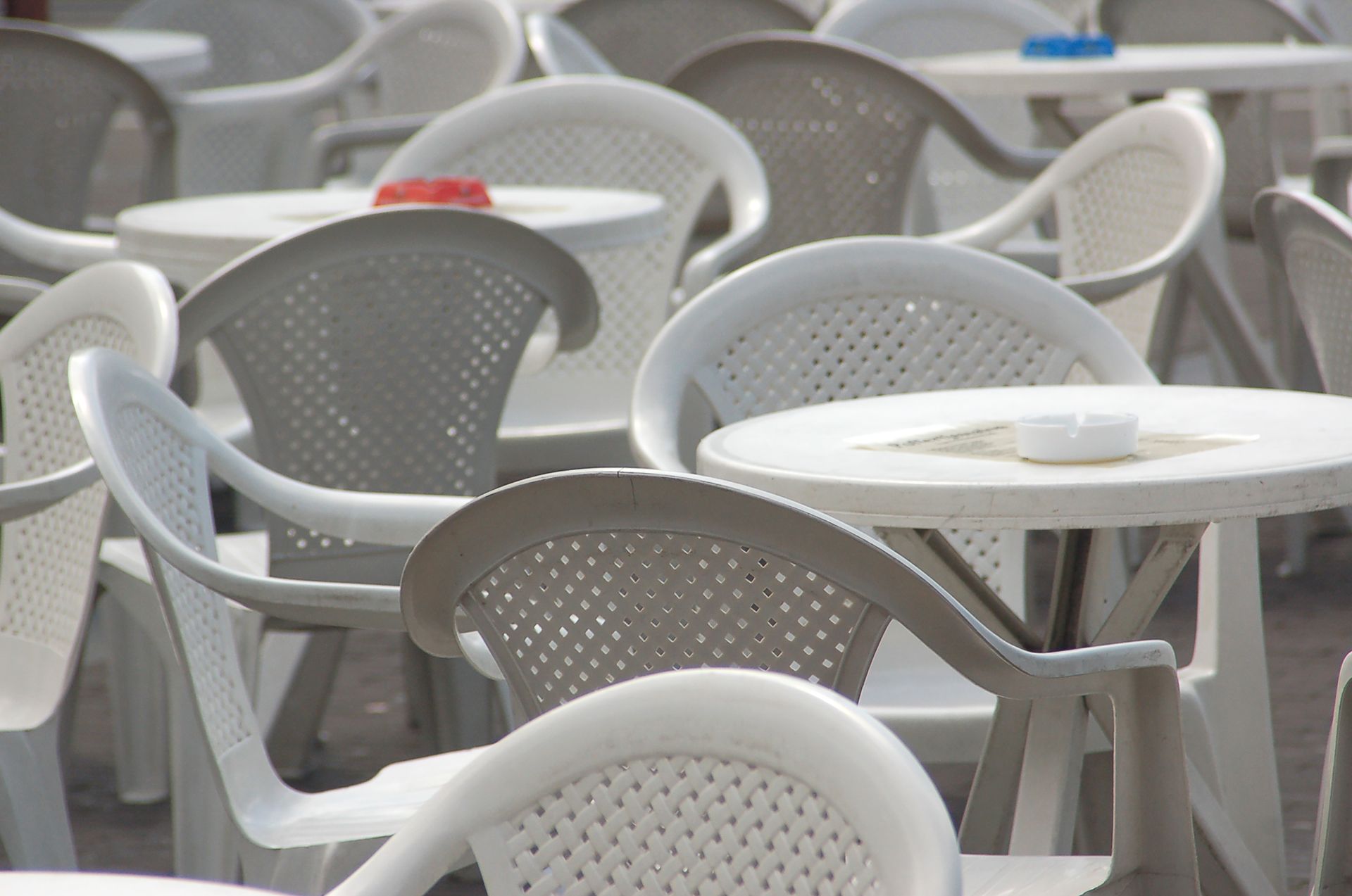 An arrangement of white plastic chairs and tables in an outdoor seating area, ideal for cafes.