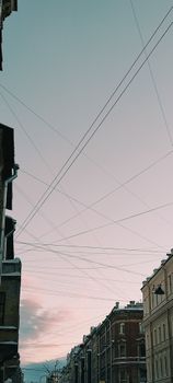 A cityscape featuring buildings and crisscrossing wires against a pastel sky, captured at dusk.