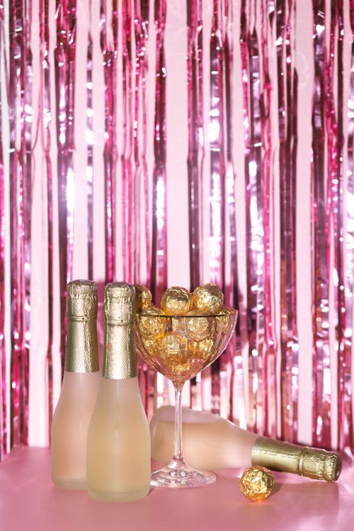 Free Chic celebration setup with champagne bottles and golden chocolates against a pink backdrop. Stock Photo