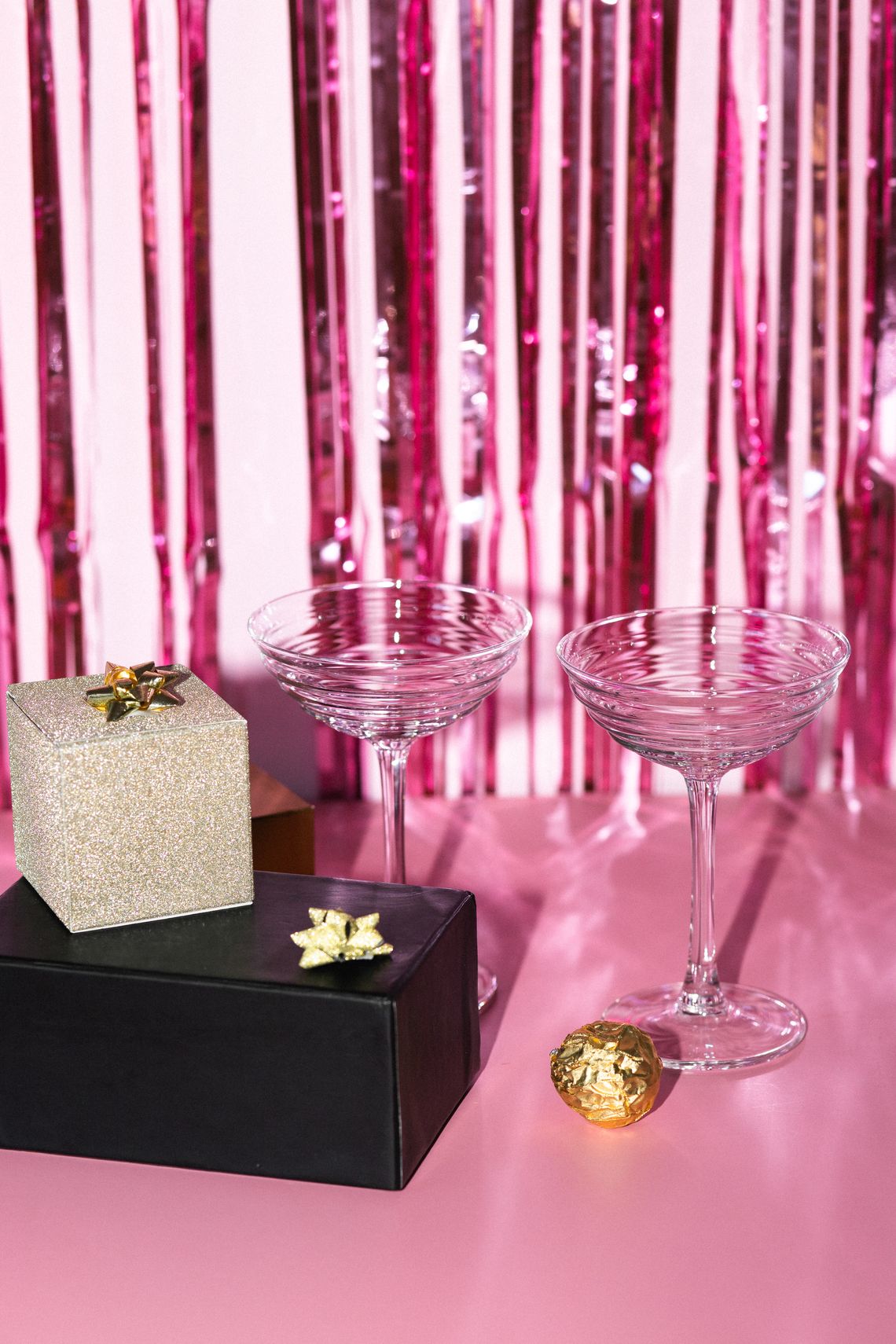 Elegant party arrangement with gift boxes and coupe glasses on a festive pink backdrop