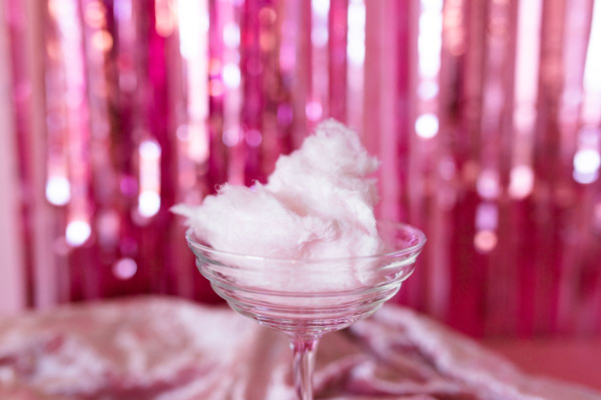 Delicate pink cotton candy elegantly presented in a clear glass against a festive pink backdrop.