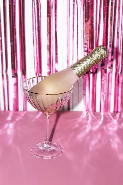Bottle of Champagne in a Cocktail Glass on a Table against Pink Background 