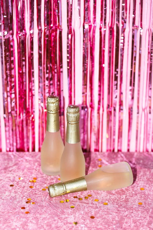 Champagne Bottles on Pink Surface with Gold Confetti 
