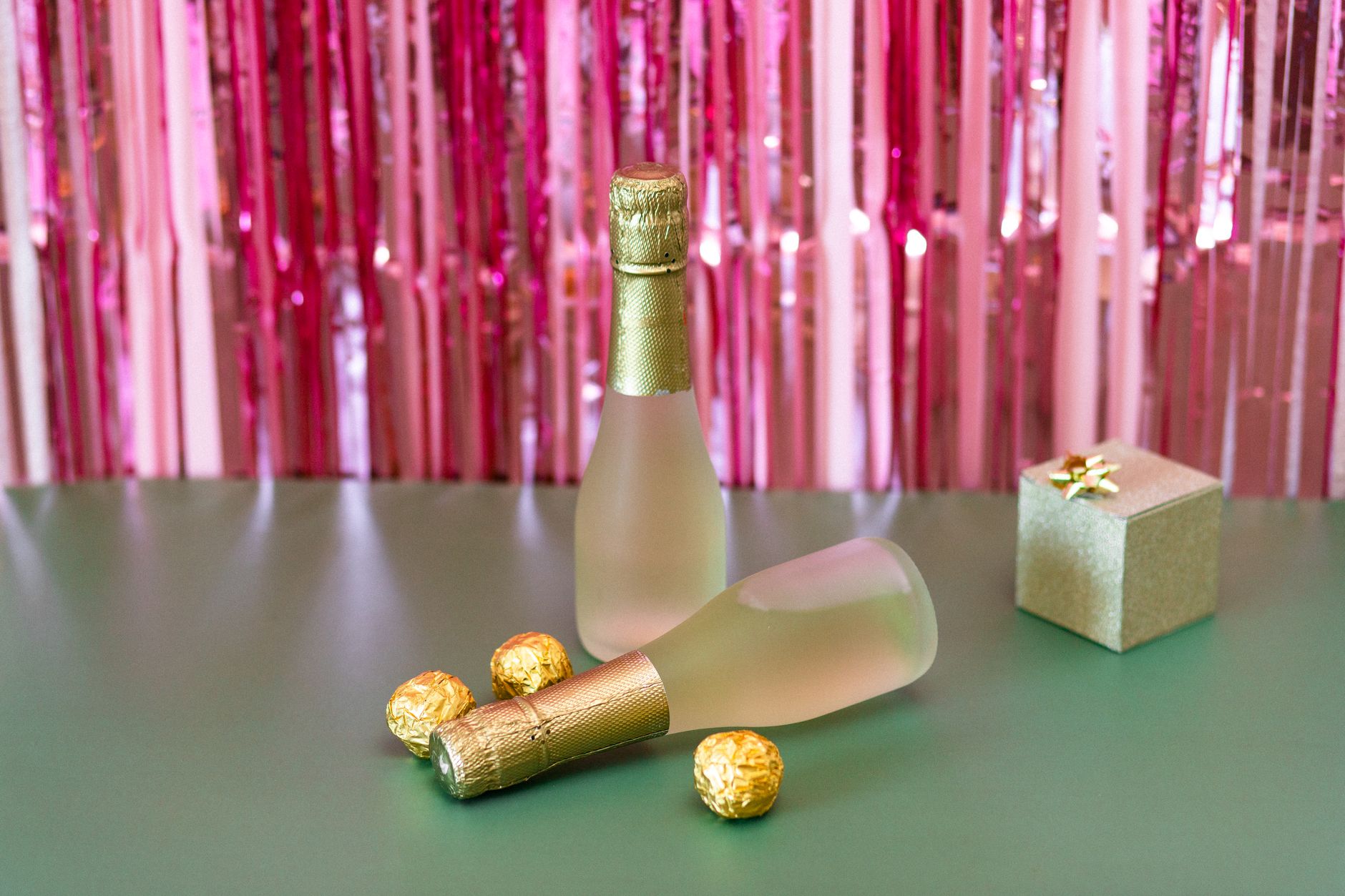Pink festive backdrop with champagne bottles, chocolates, and a gift box.
