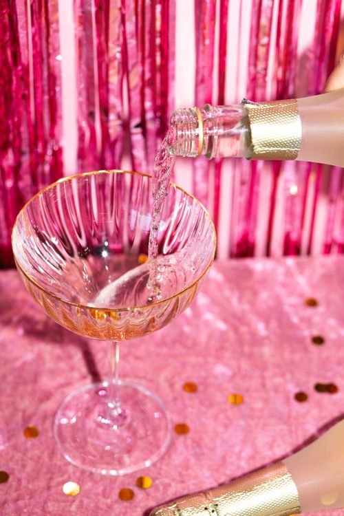 Free Close-up of champagne being poured into a crystal glass against a festive pink backdrop. Stock Photo