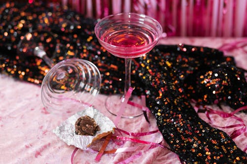 A Sequin Fabric, Cocktails Glass and a Chocolate on a Table against Pink Background 