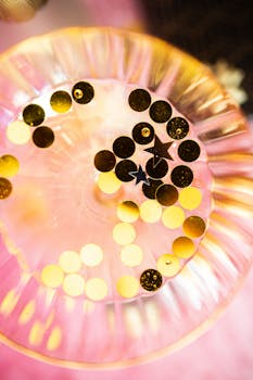 Top view of a glass with golden and black confetti on a pink background, perfect for celebrations.