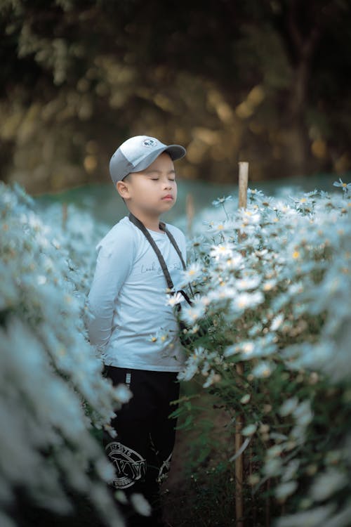 A Young Boy in White Sweater Standing on a Flower Field with His Eyes Closed