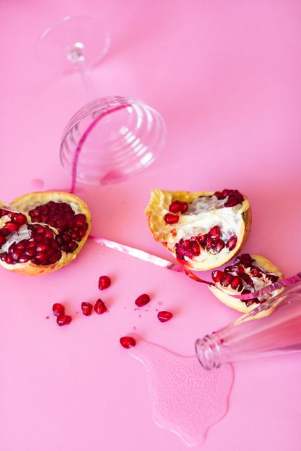 A pomegranate sliced into quarters on a wooden board with a bowl of loose ruby-red arils sitting beside it