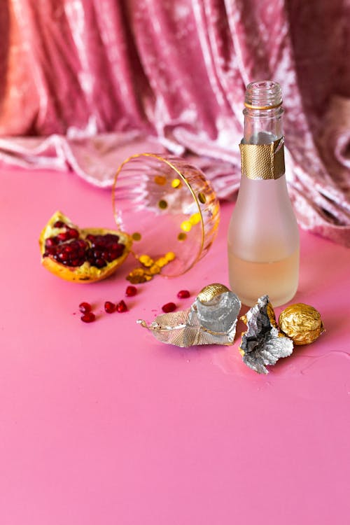 Empty Bottles, Cocktail Glass and Leftover Food Lying on Pink Surface