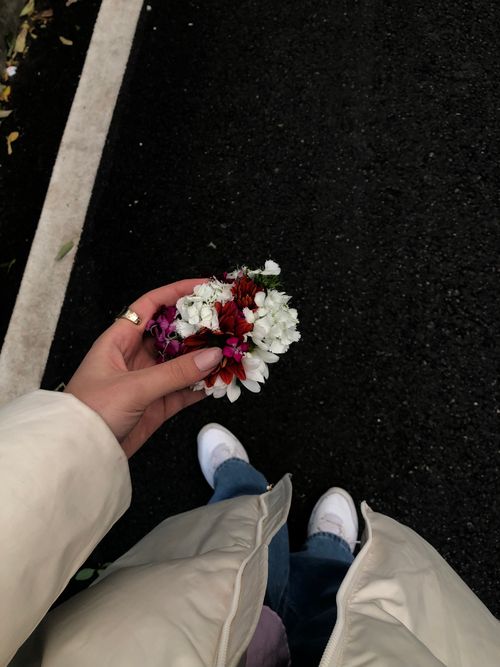 Free A person in casual attire holding vibrant flowers on a dark street pavement. Stock Photo