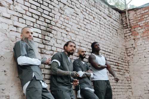 Free Four men in casual attire leaning against a brick wall outdoors, showcasing diverse styles. Stock Photo