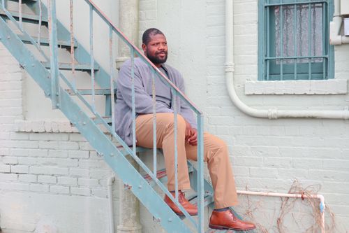 Free A contemplative man in a sweater sits on a metal staircase against a brick wall. Stock Photo