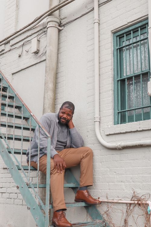 Free Man in casual clothing sits thoughtfully on outdoor stairs against a brick wall. Stock Photo
