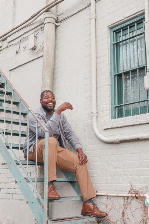 Free A joyful man sitting on stairs outside a brick building, wearing casual clothes. Stock Photo