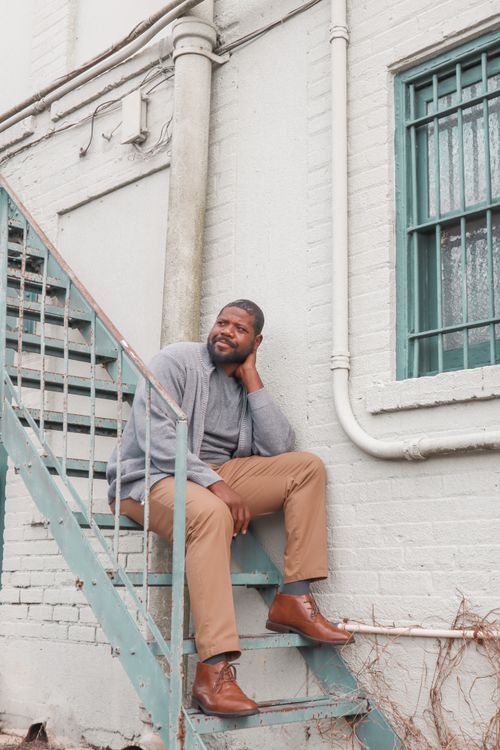 Free Man with short hair sits casually on outdoor industrial staircase, urban setting. Stock Photo