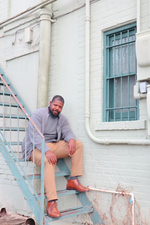 Free A man sits on metal stairs outside a building, conveying a relaxed, urban vibe. Stock Photo