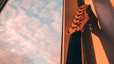 窗外，一把电吉他的琴颈在日落天空的风景中投下阴影
