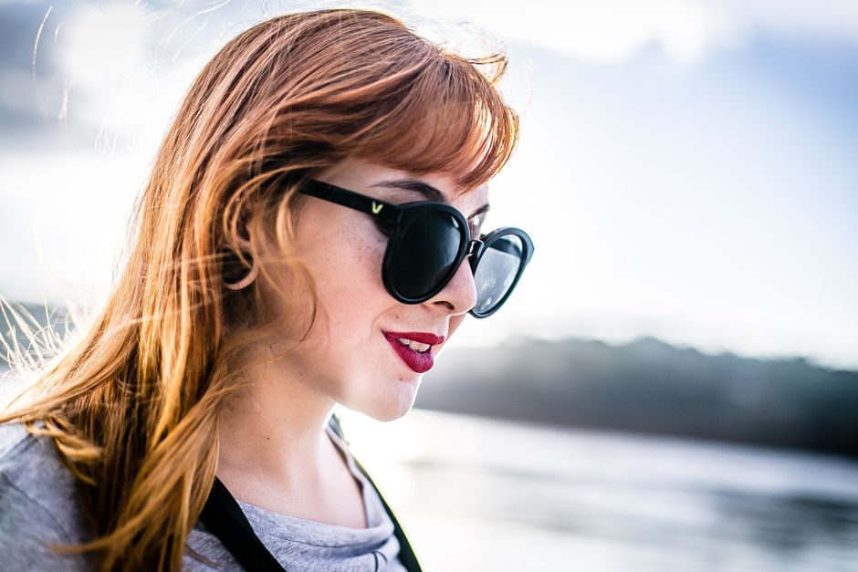 A young woman with blonde hair and sunglasses enjoying a sunny day by the lake.
