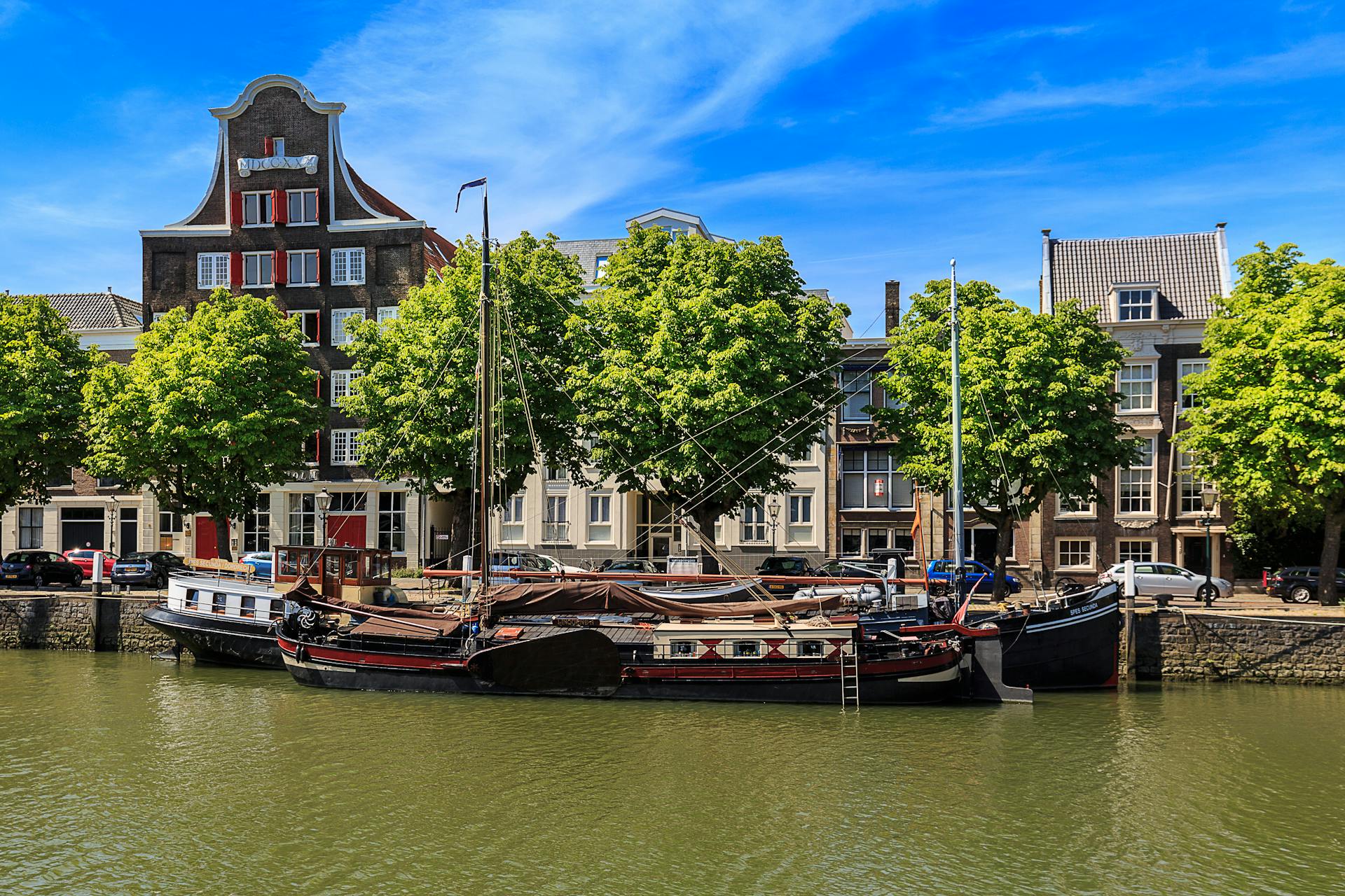 Charming scene of historic ships moored along Dordrecht's canal, framed by classic Dutch architecture.