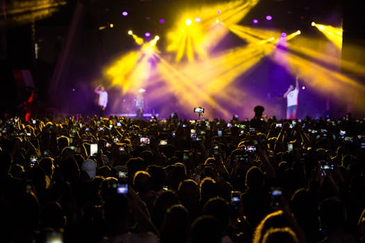 音乐会现场热闹非凡，一大群人在戏剧性的灯光下用手机记录这一刻