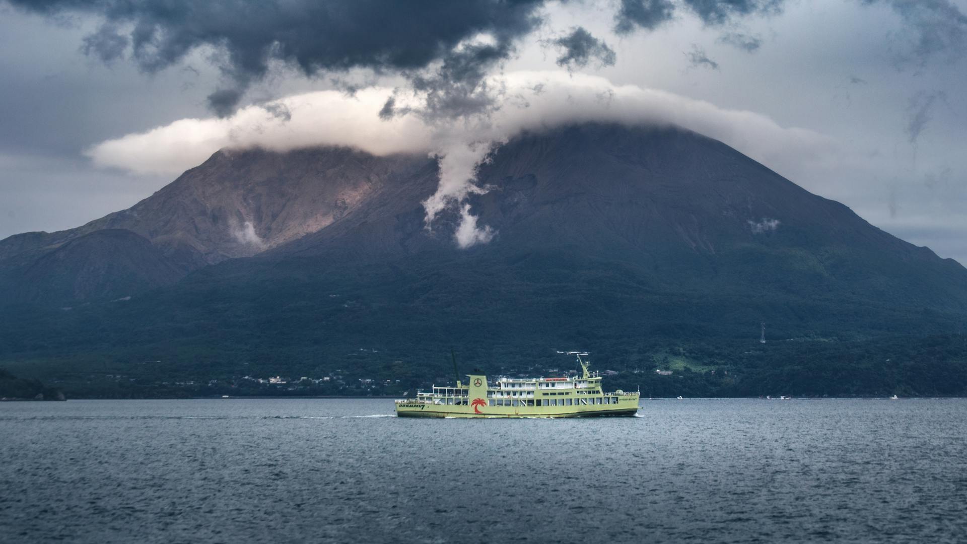 Scenic view of a ferry sailing near Sakurajima Volcano under dramatic cloud cover in Kagoshima, Japan.