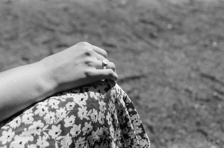 Black And White Photo Of Hand Wearing Engagement Ring Resting On Knee