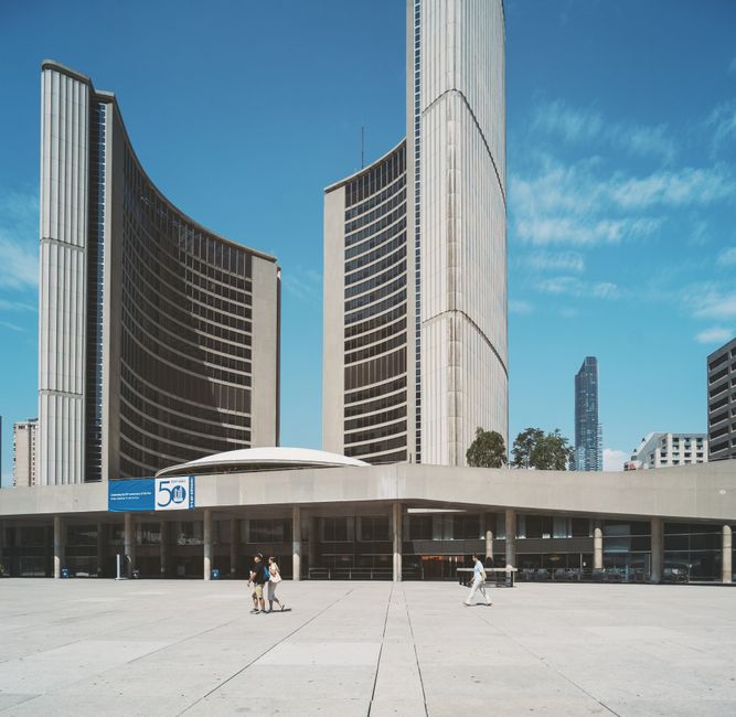 Iconic Toronto City Hall with adjacent buildings under a clear blue sky, capturing urban architecture.