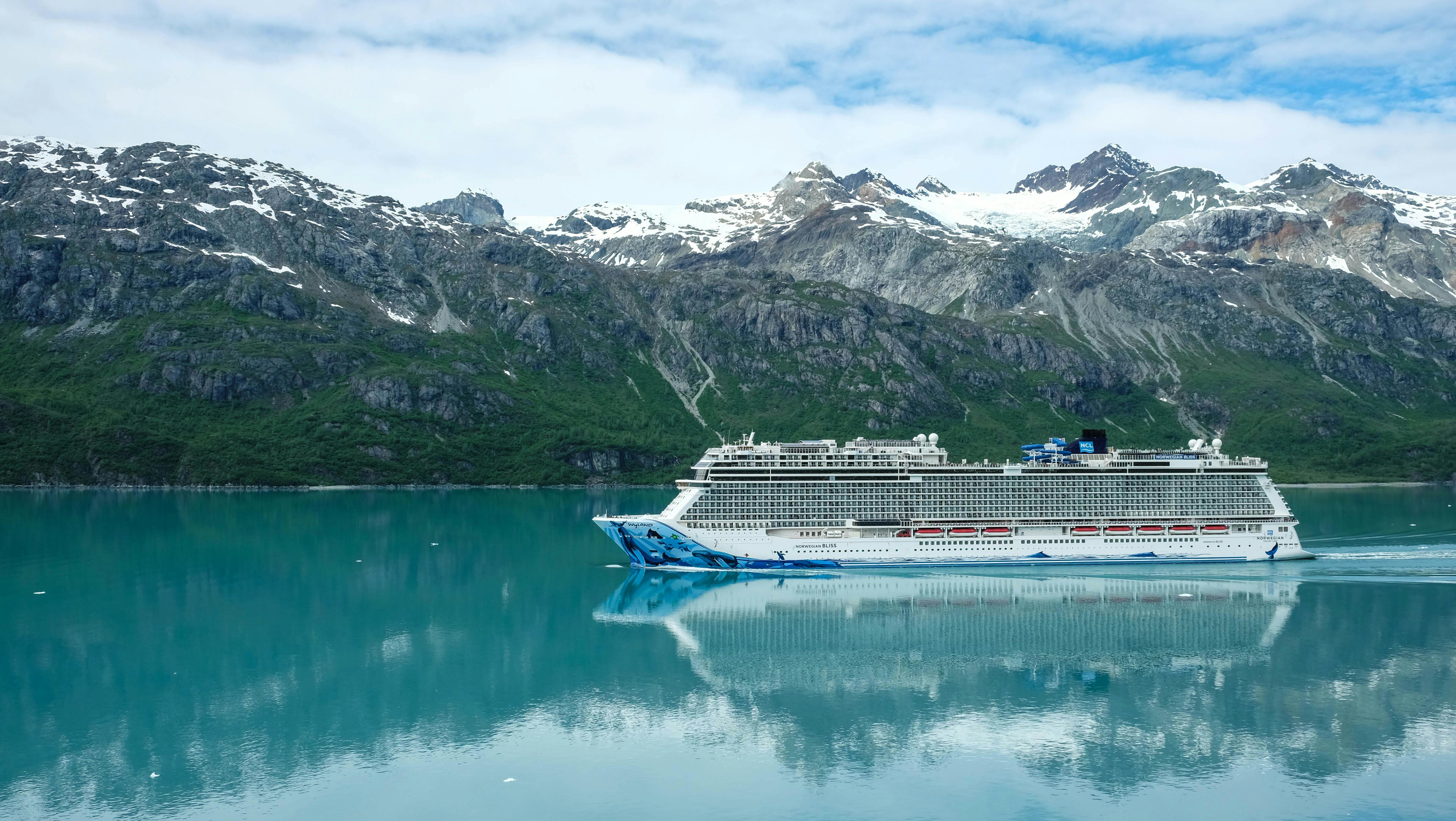 A majestic cruise ship sailing through clear waters with snowy mountains as a backdrop.