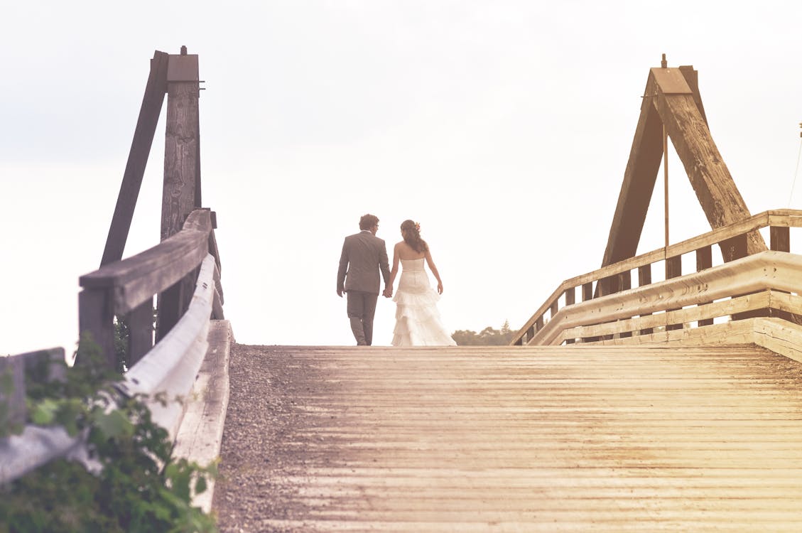 Man and Woman Holding Hands While Walking on Bridge