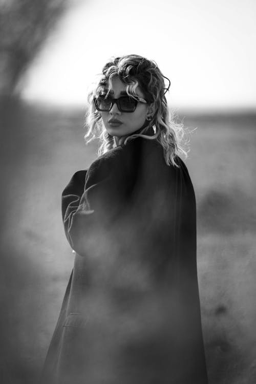 Grayscale Photo of Woman in Black Coat Wearing Sunglasses
