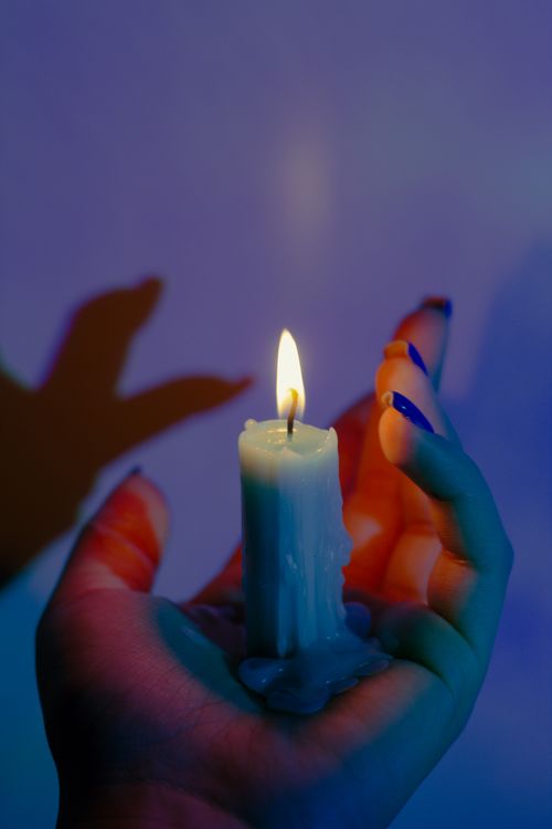 Free Artistic shot of a lit candle held in hand with colorful shadow play. Stock Photo