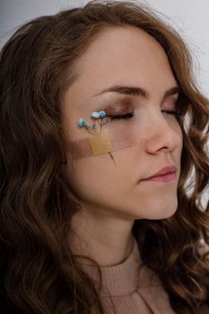 Artistic portrait of a woman with closed eyes and flowers taped to her face, highlighting creativity.