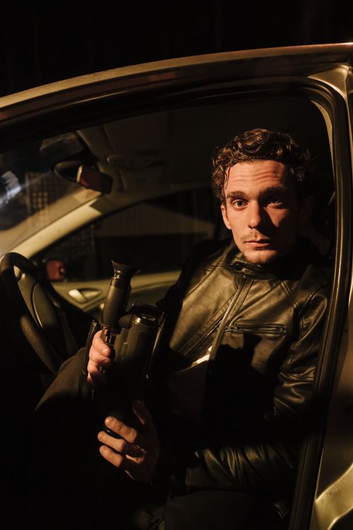Free Man wearing leather jacket sits in car, holding camcorder in a nighttime setting. Stock Photo