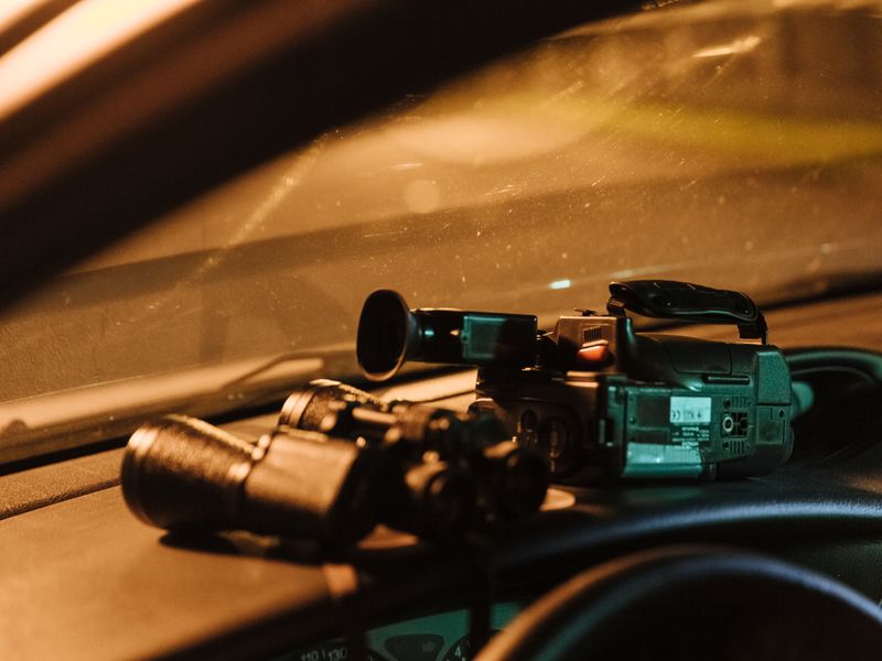 Video camera and binoculars on a car dashboard during a surveillance operation