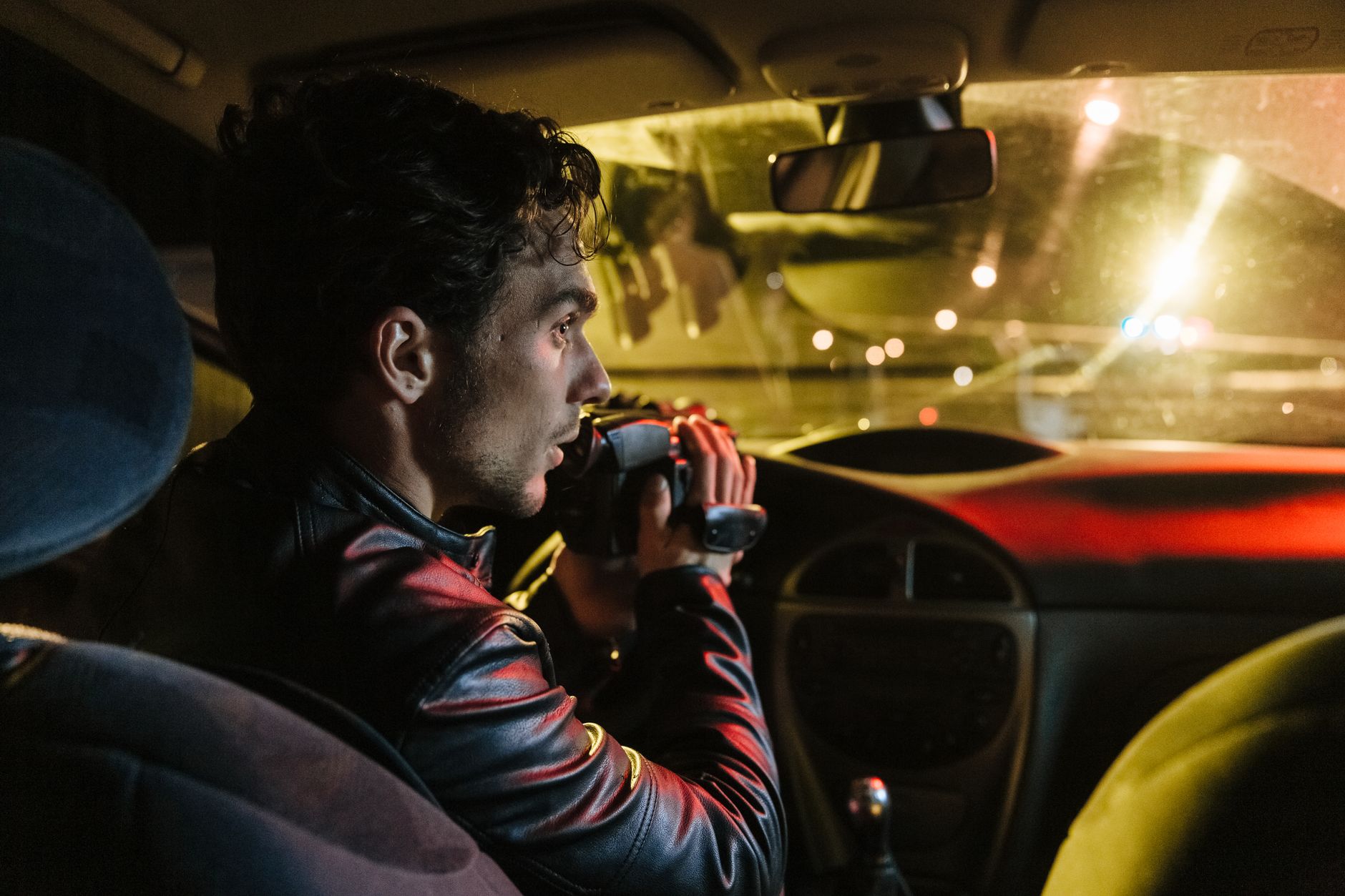 Man in a car recording outside at night using a camcorder, showcasing film-making or surveillance.