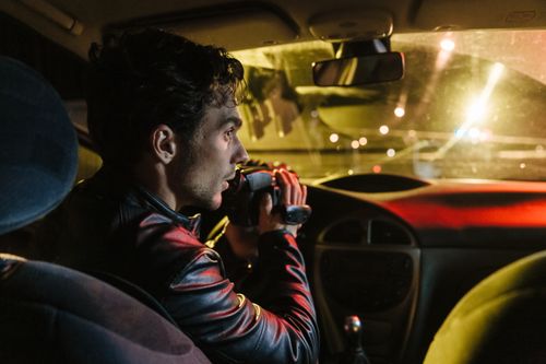 Free Man in a car recording outside at night using a camcorder, showcasing film-making or surveillance. Stock Photo