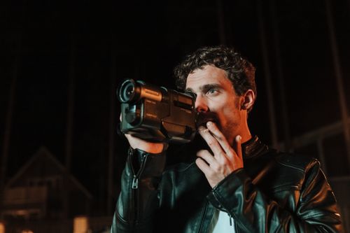 Free A man in a leather jacket smoking a cigarette while using a video camera at night. Stock Photo