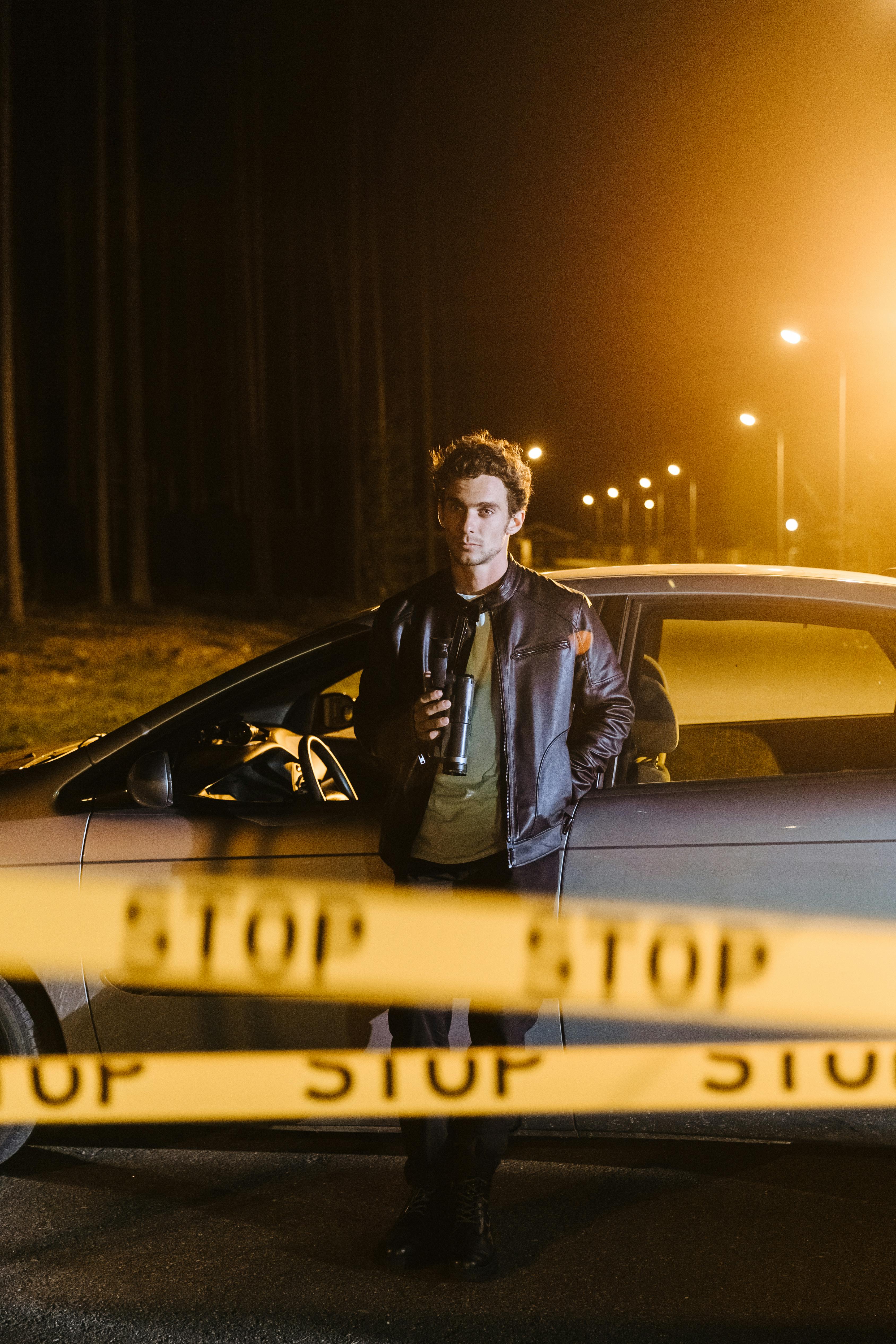 a man in black jacket standing near the car parked on the street at night