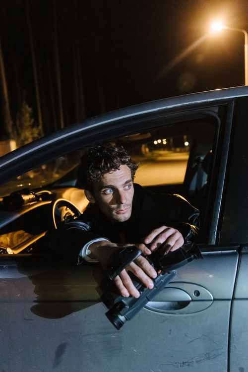 Free Man sits in car at night holding a mysterious object, illuminated by streetlights. Stock Photo