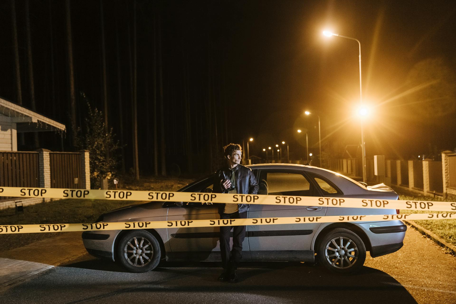 A Man Standing Beside Car Near Barricade Tapes Holding a Camcorder