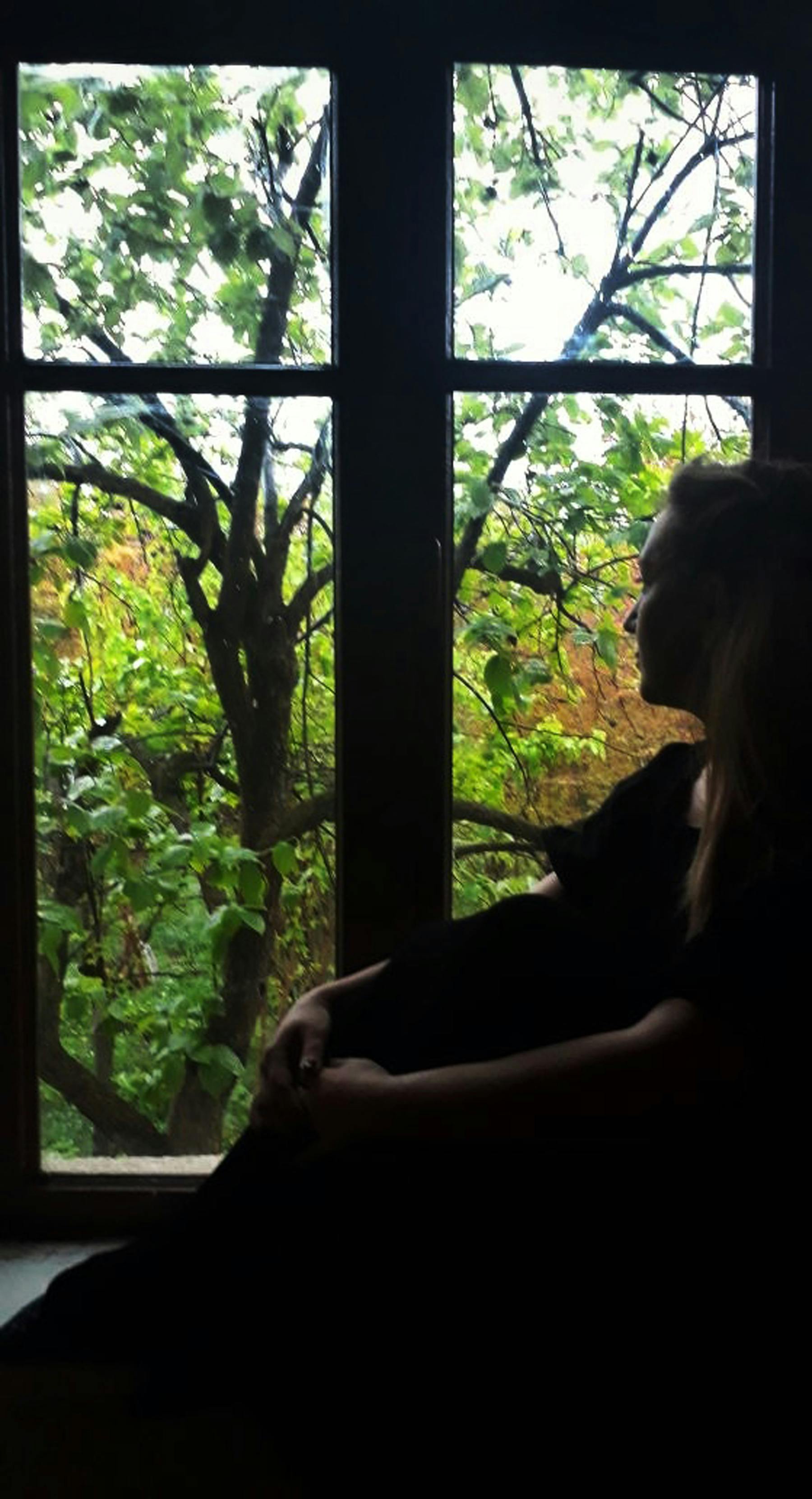 Sensual couple in close embrace on bed, man whispering intimately, rain-streaked window with autumn leaves, cozy erotic tension and trust