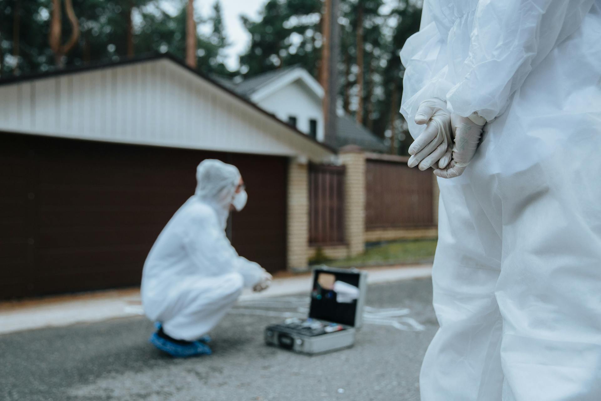 Forensic investigators in white suits and masks examining a crime scene outside a residential area.