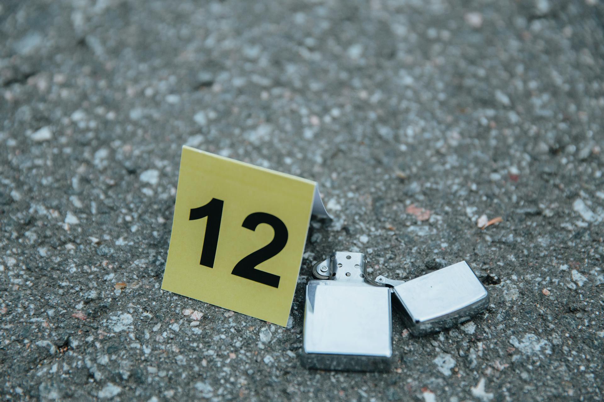 A detailed close-up of a lighter at a crime scene marked with an evidence number sign on concrete.